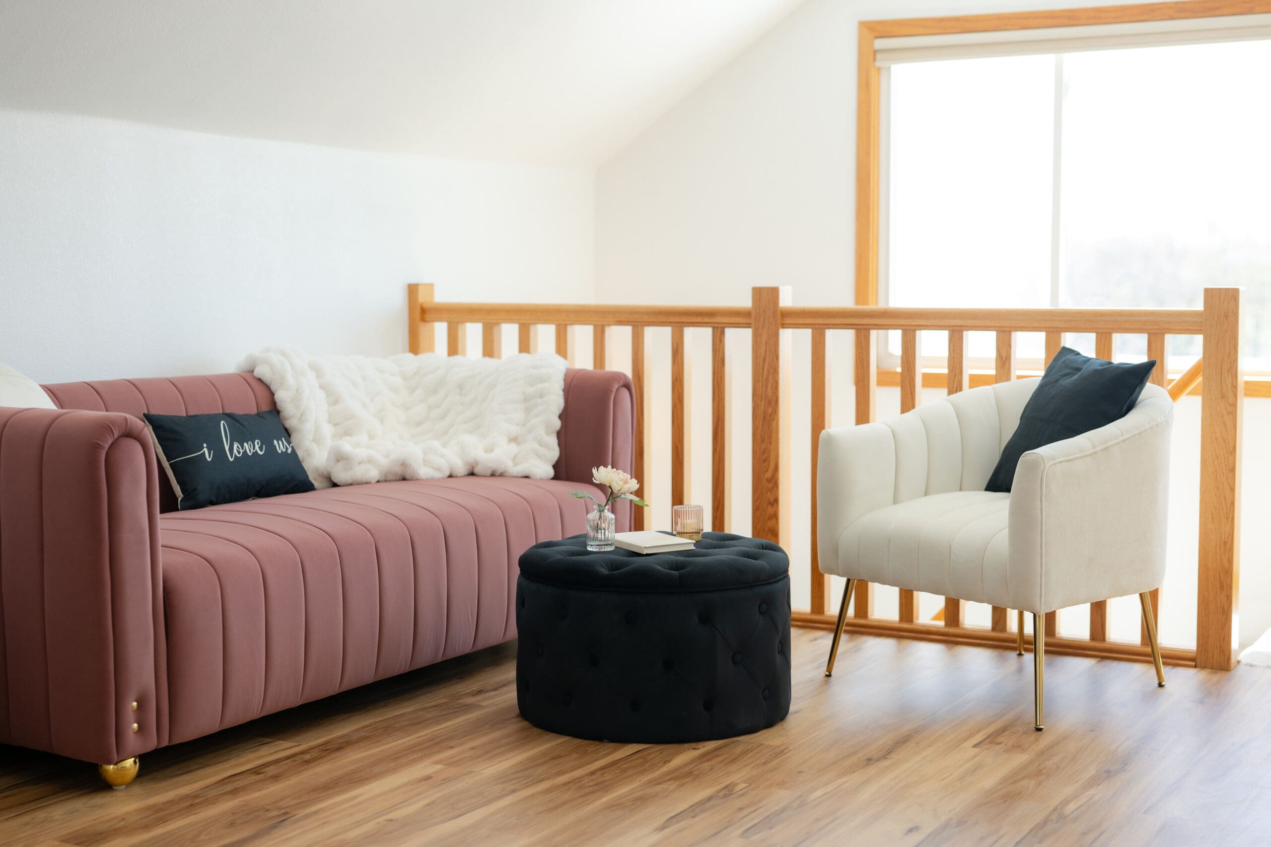 The lounge area of The Era's Luxury Bridal Loft with a dusty rose velvet sofa, tufted black ottoman, cream accent chair, and warm natural light from a large window.