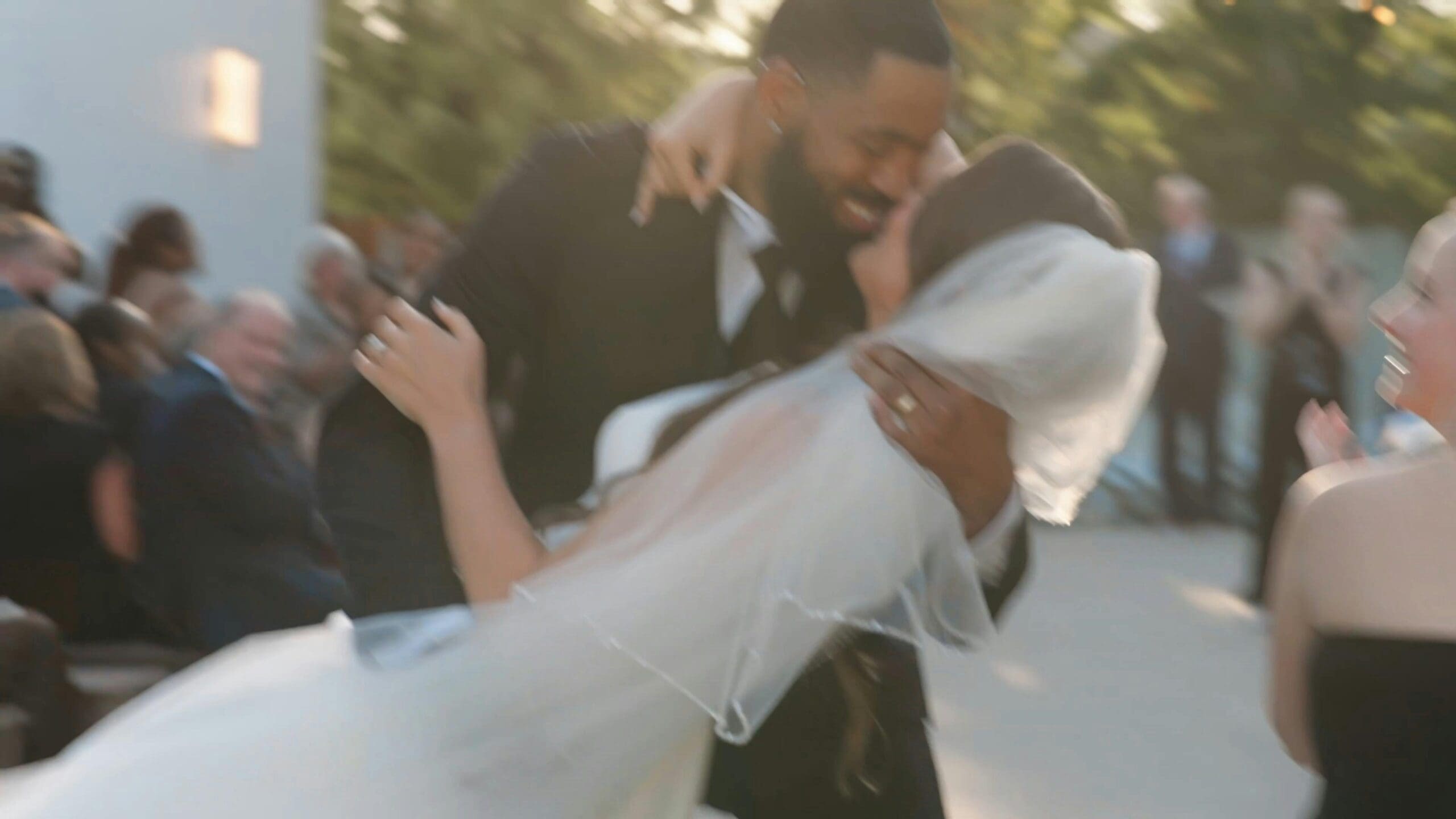 A groom dipping his bride during a joyful outdoor wedding ceremony while guests cheer and applaud at an Iowa wedding venue.