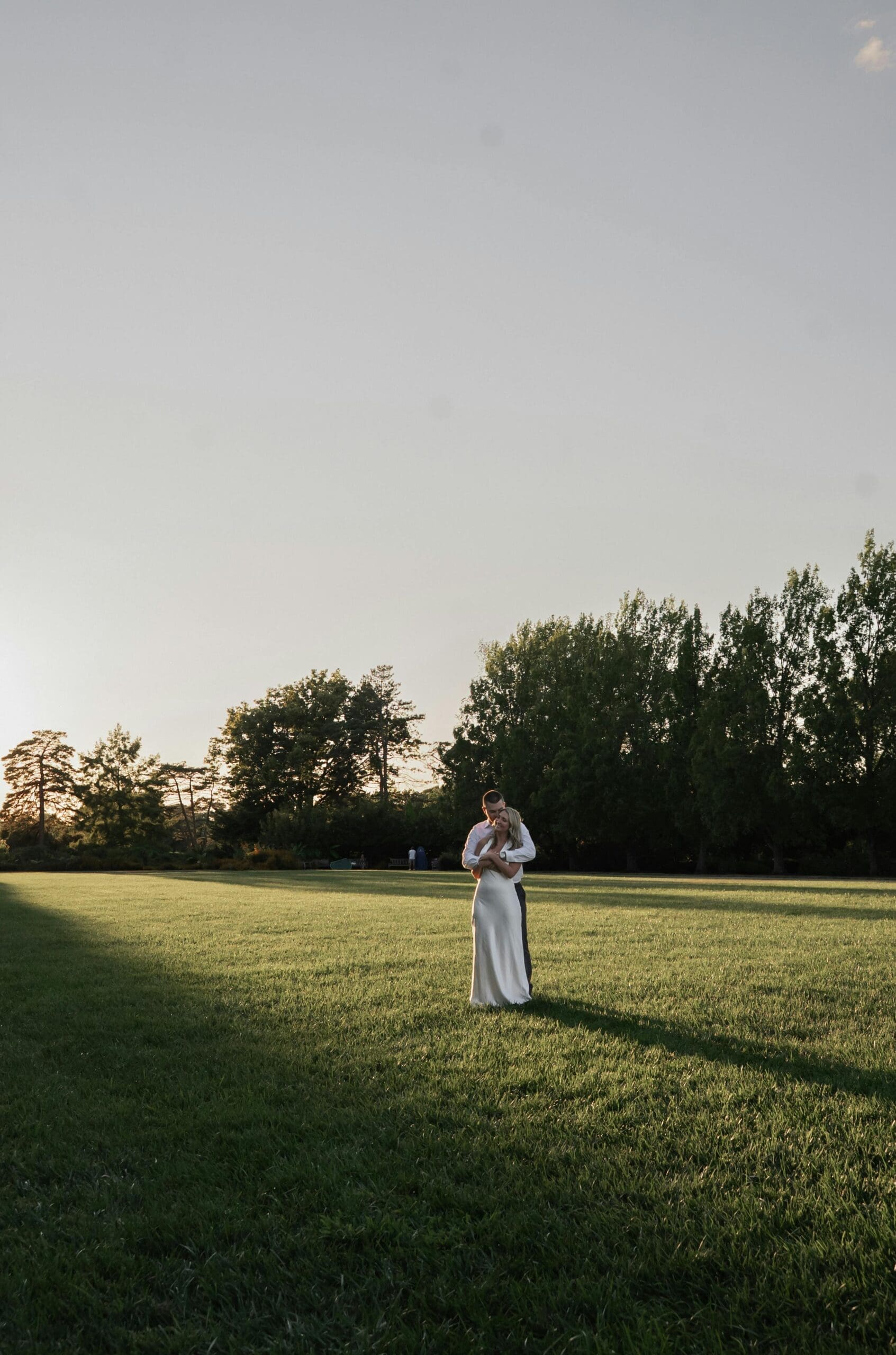 A bride and groom embracing in a wide open green field at golden hour during outdoor wedding portraits at a Midwest wedding venue.