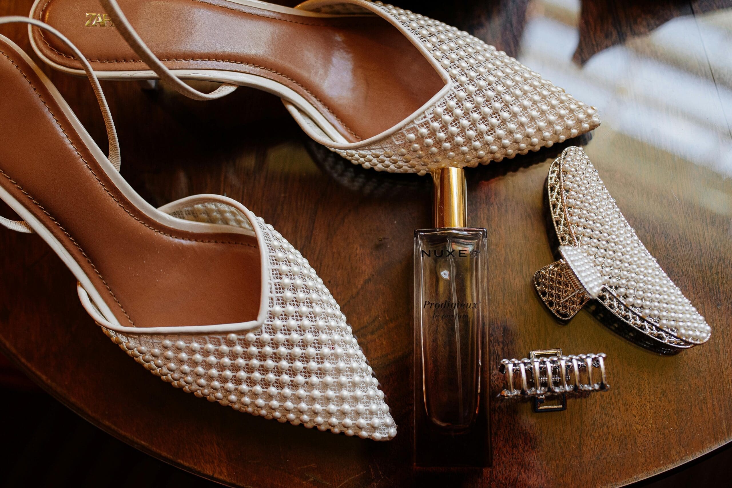 Pearl-embellished bridal heels and accessories laid out on a wooden surface in a wedding getting-ready suite.