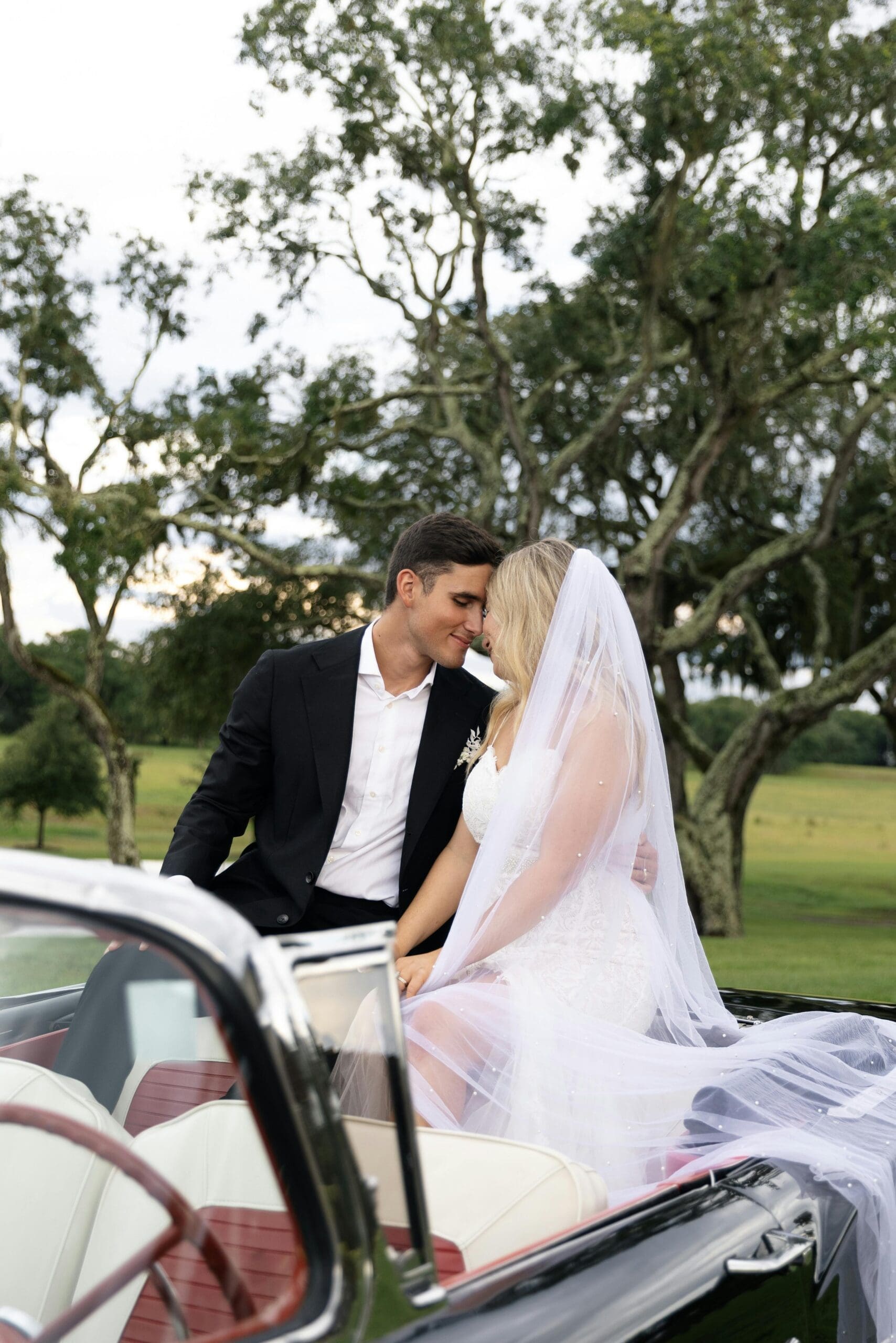 A bride and groom sitting close together in a vintage convertible during golden hour portraits on the grounds of a wedding weekend venue.