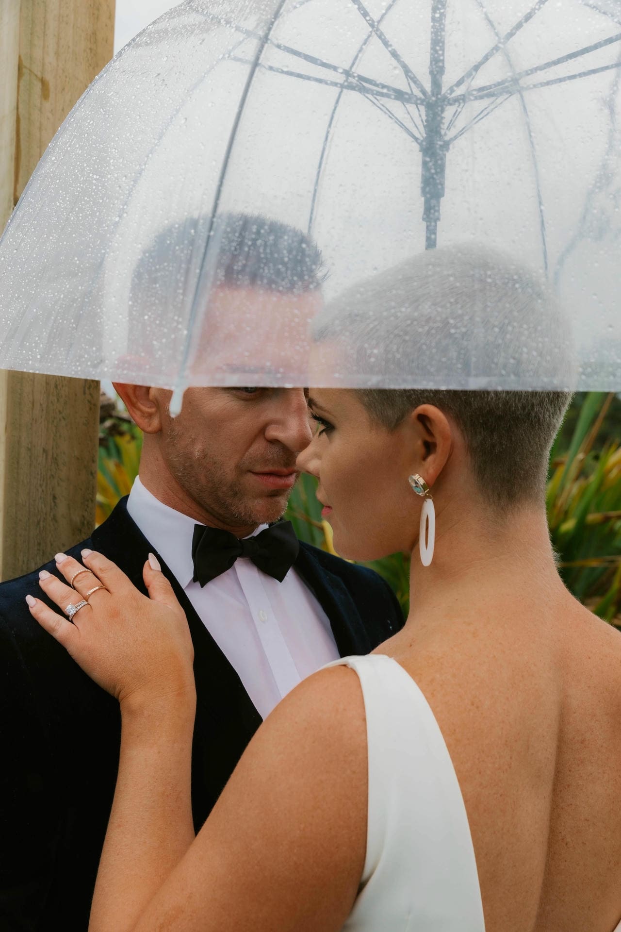 Bride and groom standing close under a clear umbrella on a rainy wedding day