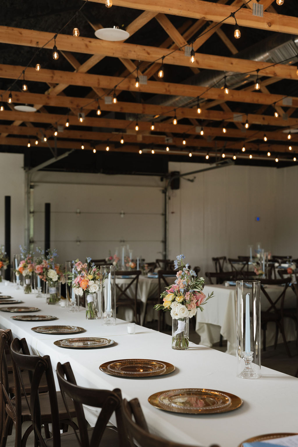 Long reception table with string lights, gold chargers, and floral centerpieces at The Era