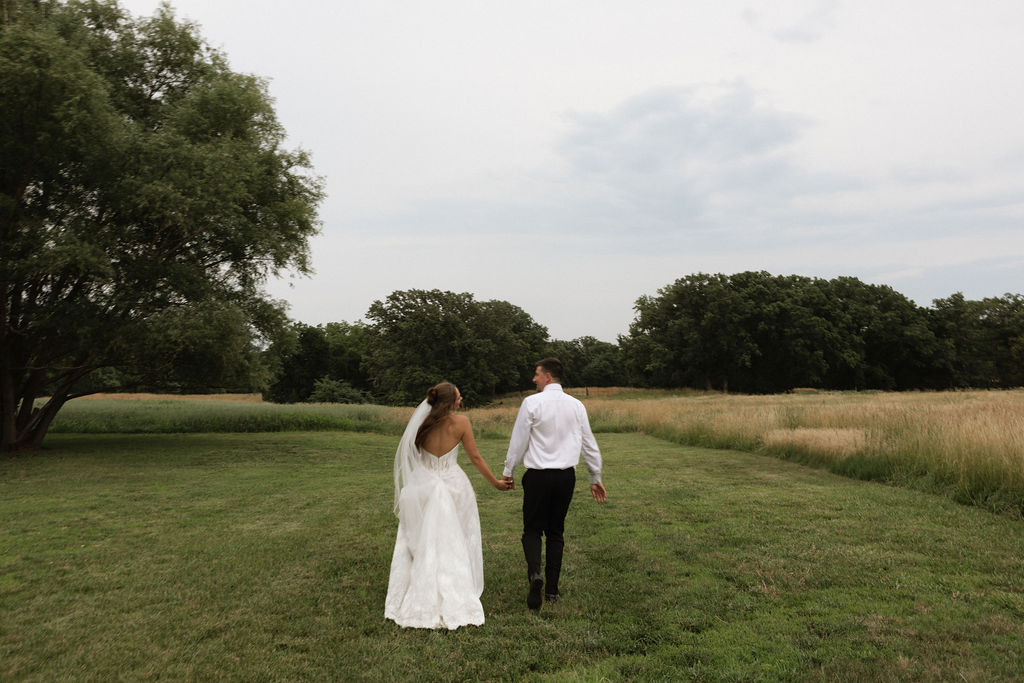 Bride and groom walking hand in hand through an open field at an Iowa wedding venue