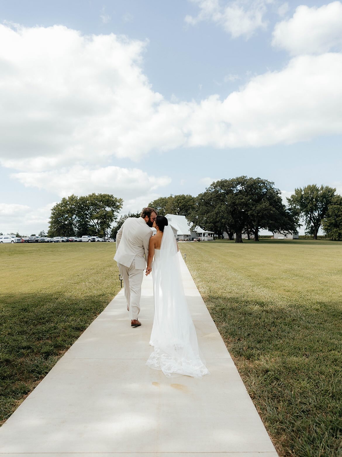 Bride and groom walking toward The Era with open Iowa landscape and sky visible