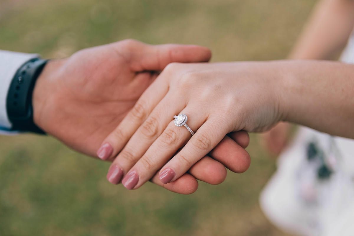 Newly engaged couple holding hands outdoors, showcasing pear-shaped halo diamond engagement ring during the first days after getting engaged