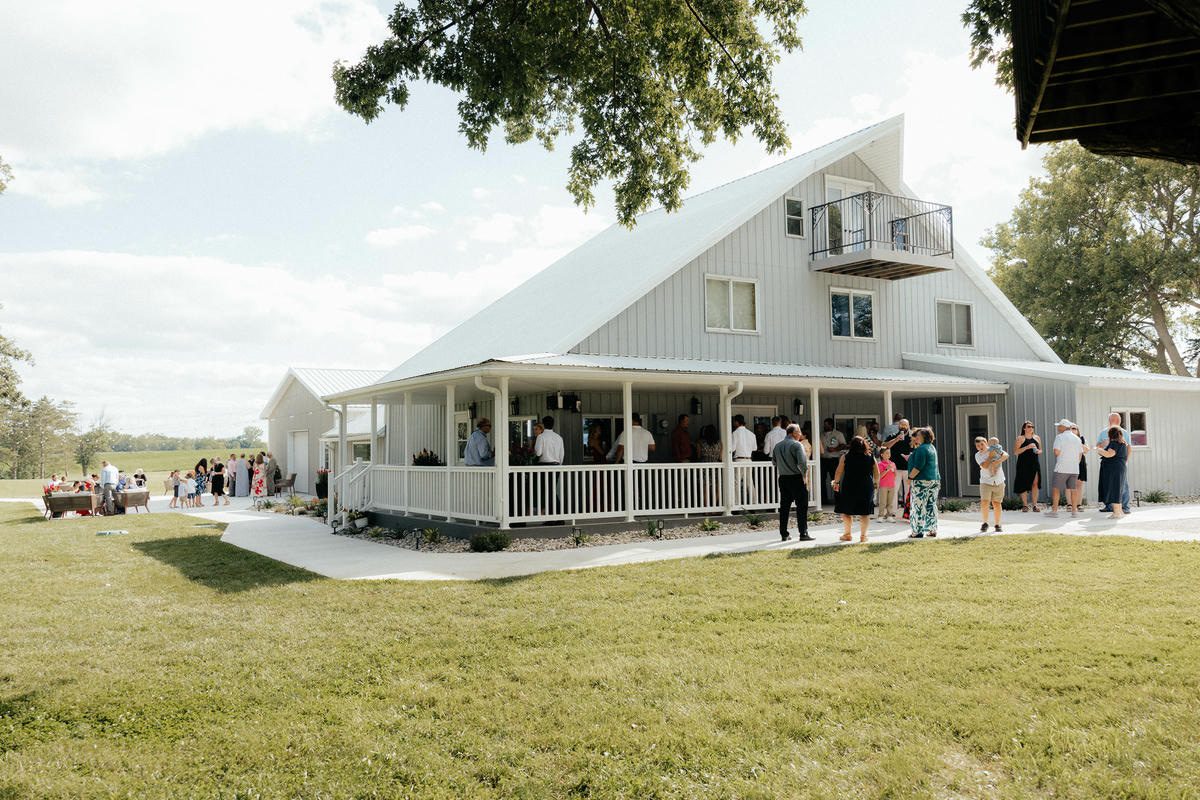 Wedding guests gathered on the porch and lawn at The Era, a full weekend wedding venue near Ames, Iowa